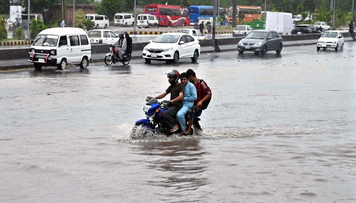 Residents in vehicles and motorcycles pass through rain water accumulated on IJP Road after heavy rain in Islamabad on July 10, 2024. — APP