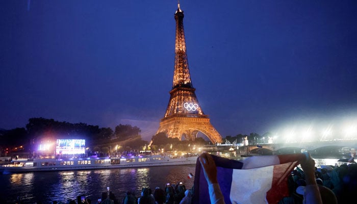 A spectator holds up French flag in front of Eiffel Tower with Olympics logo placed on it on the openening ceremony of Olympics in Paris, France in this image released on July 27, 2024. — Reuters