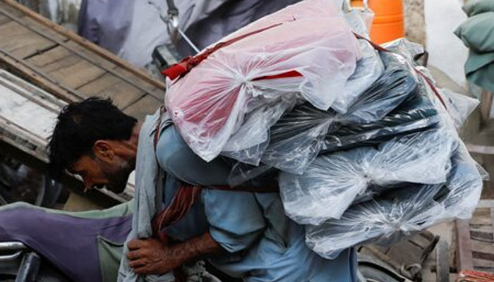 A labourer bends over as he carries packs of textile fabric on his back to deliver to a nearby shop in a market in Karachi, Pakistan June 24, 2022. — Reuters