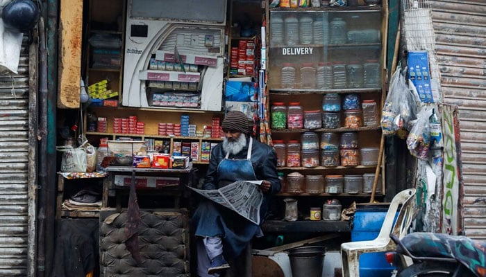 A man reads newspaper while selling betel leaves, known as pan, cigarettes and candies from a shop in Karachi, Pakistan, December 30, 2021. — Reuters