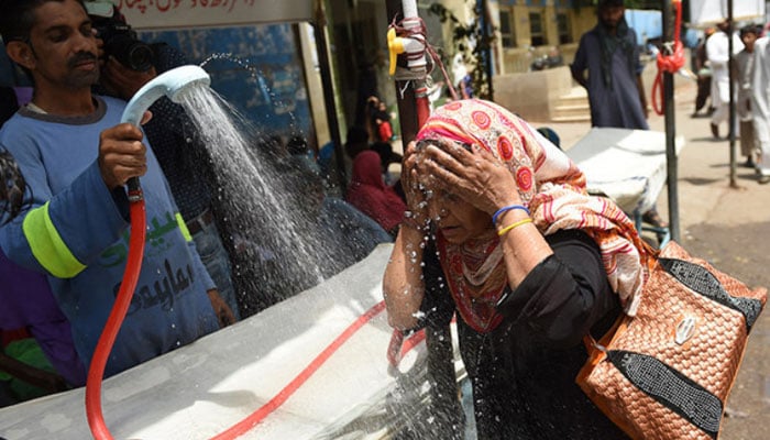 A volunteer showers a woman with water during a heatwave in Karachi. — AFP/File