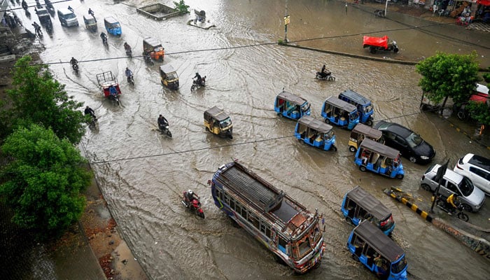 People wade through a flooded street amid rainfall in Karachi on July 30, 2024. — AFP