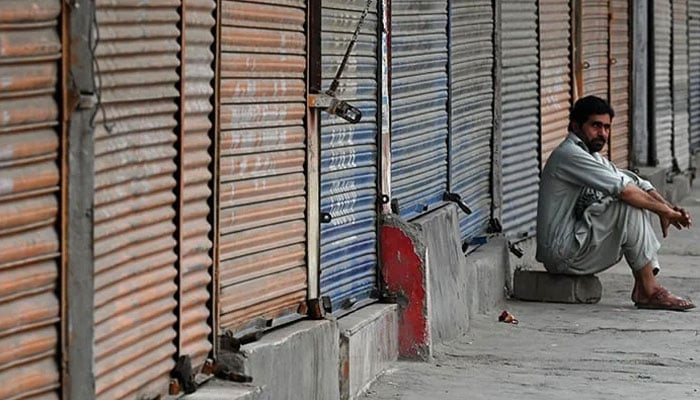 A man sits in front of closed shops along a roadside during a nationwide strike by traders against the surge in electricity and fuel prices on September 2, 2023. — AFP