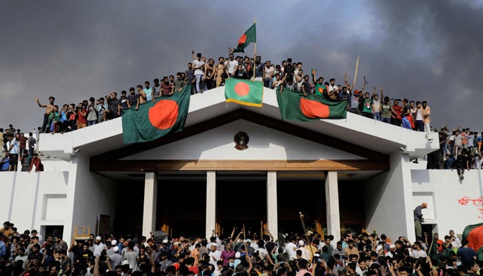 Anti-government protesters display Bangladeshs national flag as they storm now-former prime minister Sheikh Hasinas palace in Dhaka on August 5, 2024. — AFP