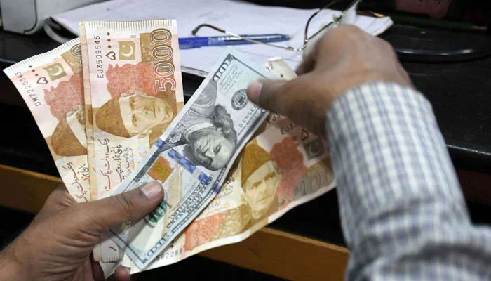 A money changer is seen holding curency notes of Pakistan and US dollars. —APP/File