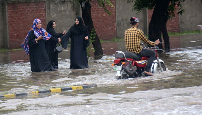 A motorcyclist passes through pedestrians on an inundated road in Lahore on July 21, 2022. — APP