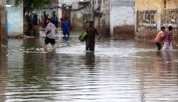 Commuters wade through a flooded road after heavy rainfall. — Online/File