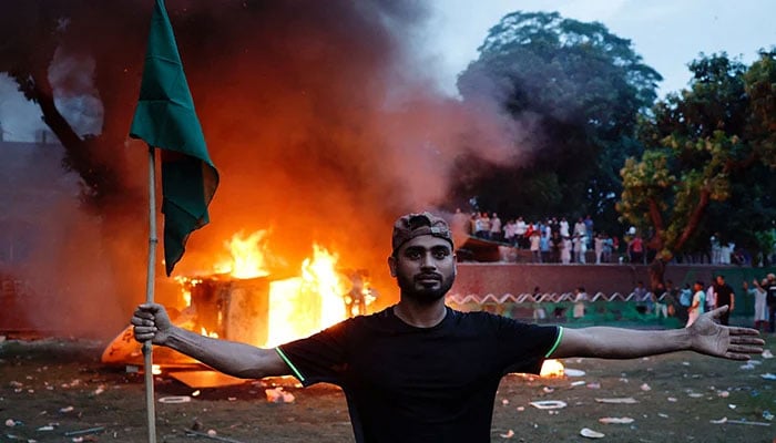 A man holding a Bangladesh flag stands in front of a vehicle that was set on fire at the the Prime Ministers residence in Dhaka, Bangladesh, August 5, 2024. — Reuters