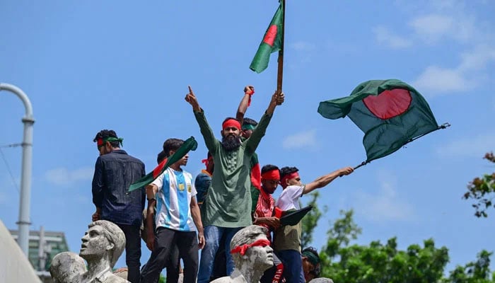 Bangladeshi protesters wave national flags as they stand over the Anti-Terrorism Raju Memorial sculpture during a protest in Dhaka, Bangladesh, on August 4, 2024. — AFP