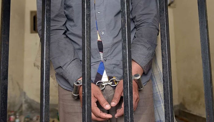 The picture shows a person handcuffed and standing behind bars. — AFP/File