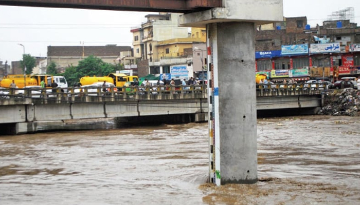 People stand on a bridge at Gawalmandi as water level in Leh Nullah rises to dangerous level. — INP/file