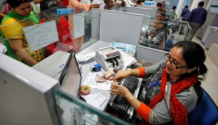 A cashier counts Indian banknotes as customers wait in queues inside a bank in Chandigarh, India on  November 10, 2016. — Reuters