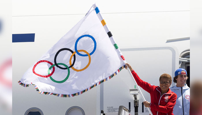 Los Angeles mayor Karen Bass (L) waves the Olympic flag next to US skateboarder Tate Carew (R) after their plane landed during an event celebrating the arrival of the Olympic flag at Los Angeles International Airport (LAX) in Los Angeles, on August 12, 2024. — AFP