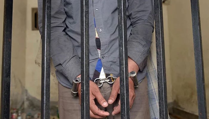 A representational image of a handcuffed person standing behind bars. — AFP/File