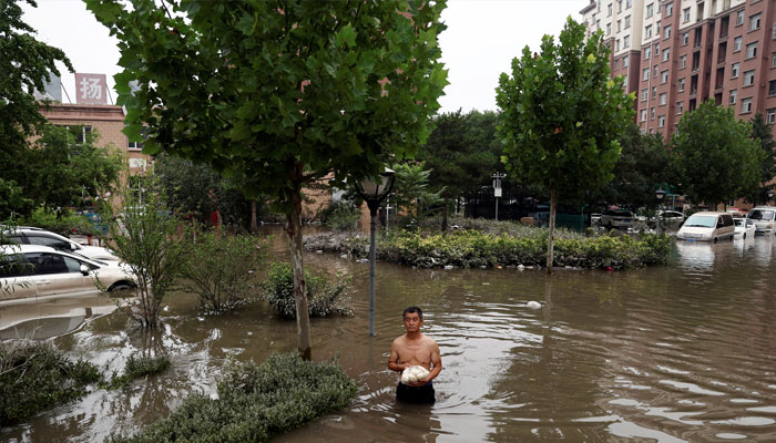 A man holding a bag of food wades through floodwaters after the rains and floods brought by remnants of Typhoon Doksuri, in Zhuozhou, Hebei province, China August 3, 2023. — Reuters