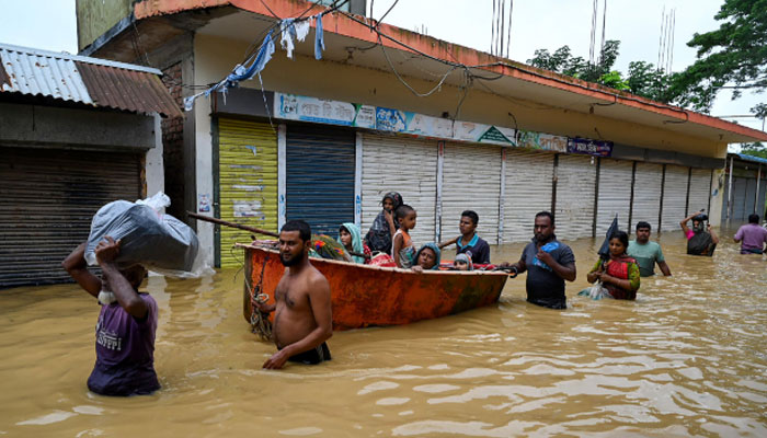 People wade through floodwaters in Bangladesh, where nearly 300,000 have taken refuge in emergency shelters. —AFP