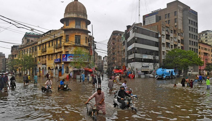 People wade across a flooded street after heavy monsoon rainfall in Karachi on July 25, 2022. — AFP