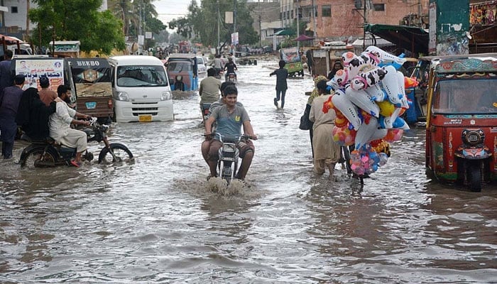 Motorcyclists passing through rainwater accumulated on a road in Korangi area of Karachi on July 9, 2022. — APP