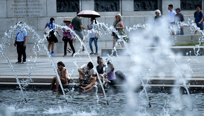 People cool off at a reflecting pool at the World War II Memorial on the National Mall in Washington, DC on August 28, 2024. — AFP