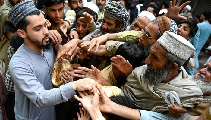 A representational image showing a person distributing bread to needy people in Peshawar. — AFP/File