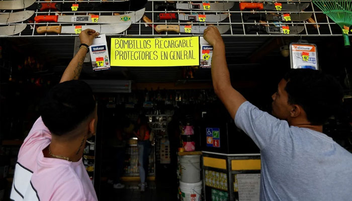 Workers put up rechargeable light bulbs for sale at a store during a blackout in Caracas on 30 August 2024. — AFP