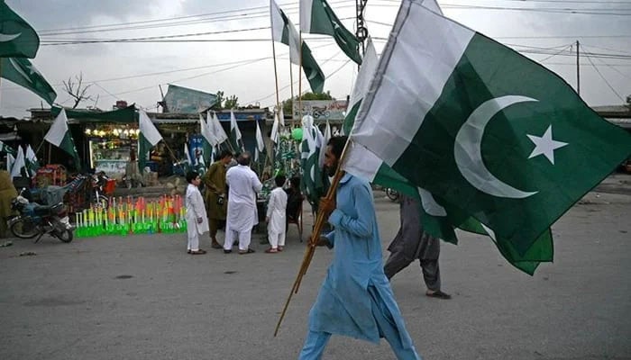 A man carrying national flags walks through a street on the eve of the Independence Day celebrations in Peshawar on August 13, 2023. — AFP