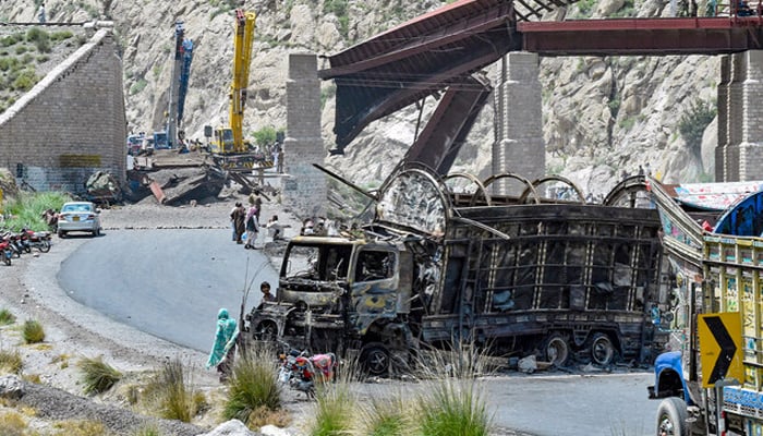 Residents stand beside a charred vehicle near a collapsed railway bridge the morning after terrorists targeted at Kolpur in Bolan district, Balochistan on August 27, 2024. — AFP