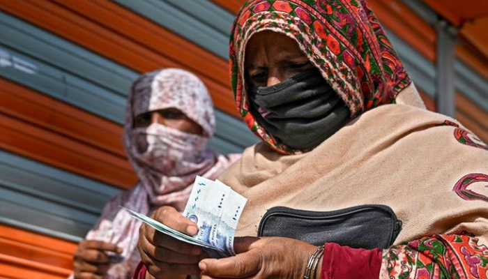 In this file photo, a woman in a face mask counts rupee notes as she walks on a street in Islamabad on April 9, 2020. — AFP