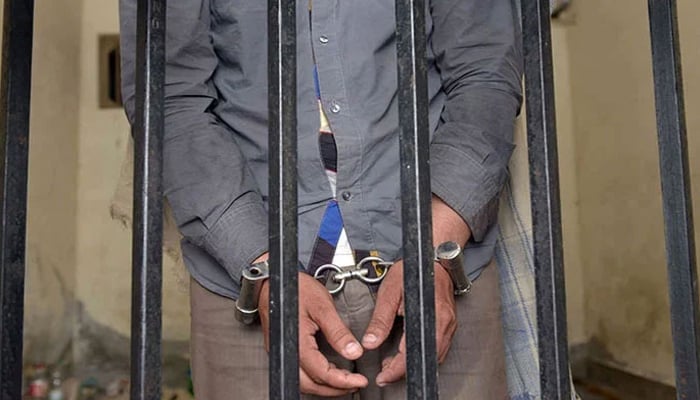 The picture shows a person handcuffed and standing behind bars. — AFP/File