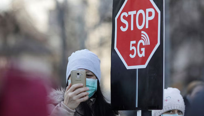 A woman uses her mobile phone while holding a placard reading  STOP 5G during a protest against 5G technology, in Bucharest, Romania on January 25, 2020. — Reuters