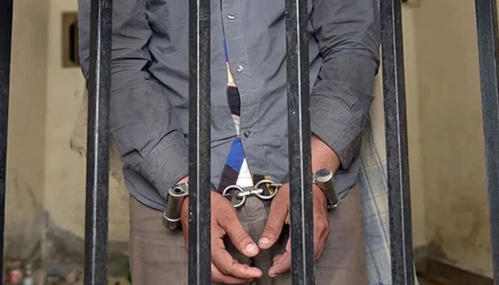 The picture shows a person handcuffed and standing behind bars. — AFP/File