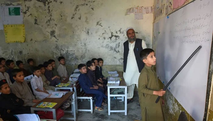 In this undated photo, a student, while holding a stick in his hand, reading a paragraph written on the black board in front of his classmates. — AFP