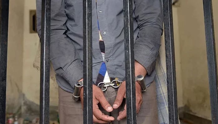 The picture shows a person handcuffed and standing behind bars. — AFP/File