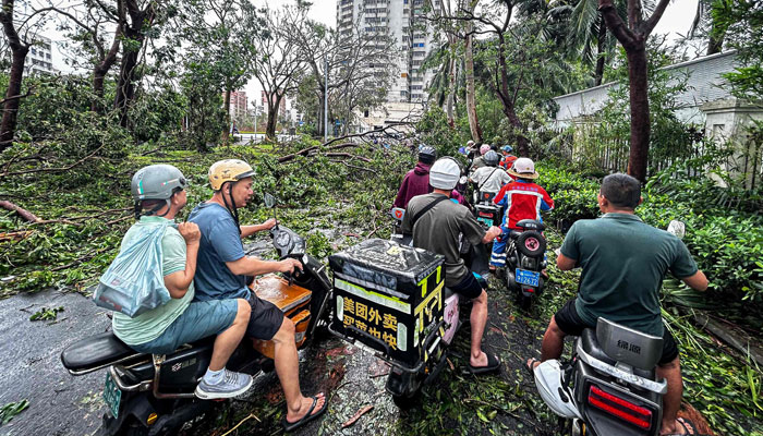 People ride scooters past falling trees after Super Typhoon Yagi hit Haikou, in southern Chinas Hainan province on September 7, 2024. — AFP