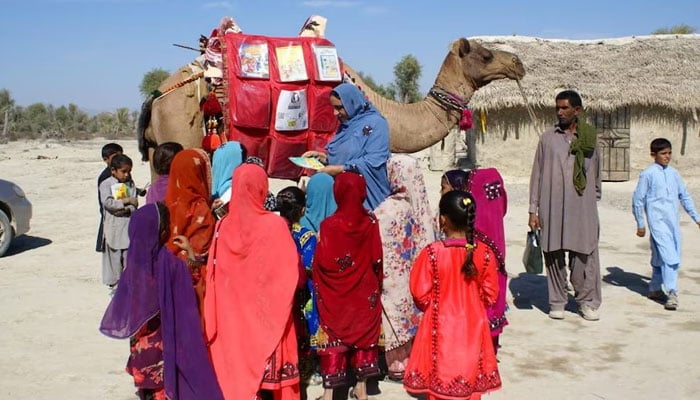 Children stand next to a camel that brought books in Mand, Balochistan on April 11, 2021. — Reuters