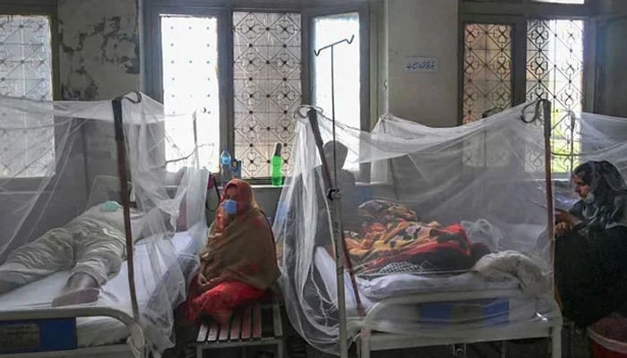 Relatives sit next to patients suffering from dengue fever at a hospital. — AFP/File