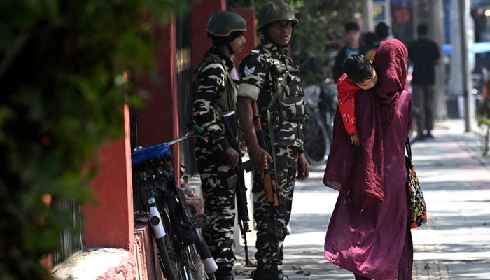 A woman along with a child walks past Indian security personnel on a street in Srinagar on September 9, 2024. — AFP