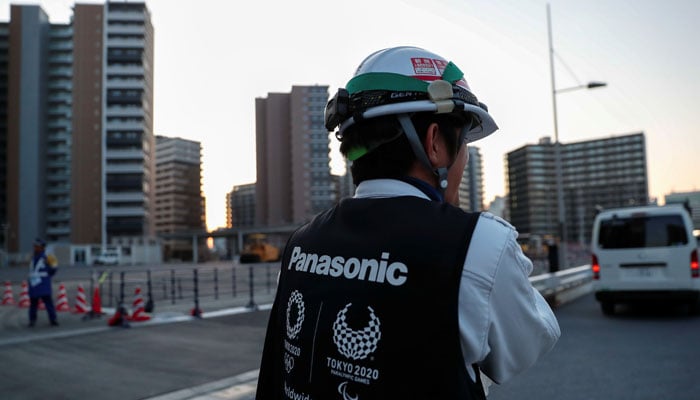 A worker wears a jacket with the logo of Panasonic, Tokyo 2020 Olympic and Paralympic Games partner, as he walks at an under-construction site of the Olympic villages in Tokyo, Japan March 25, 2020. — Reuters