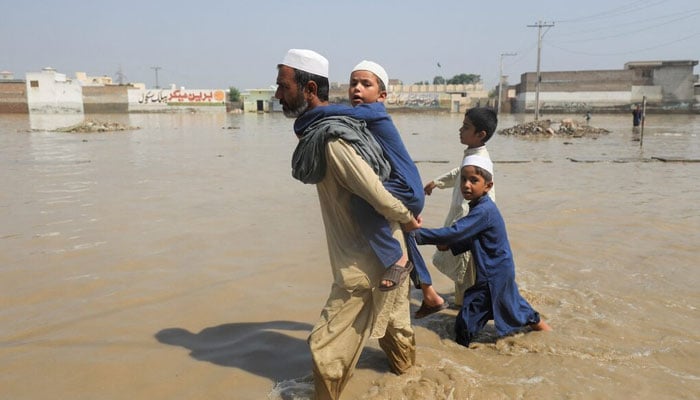 A man walks with children amid flood water along a road, following rains and floods during the monsoon season in Nowshera on August 30, 2022. — Reuters