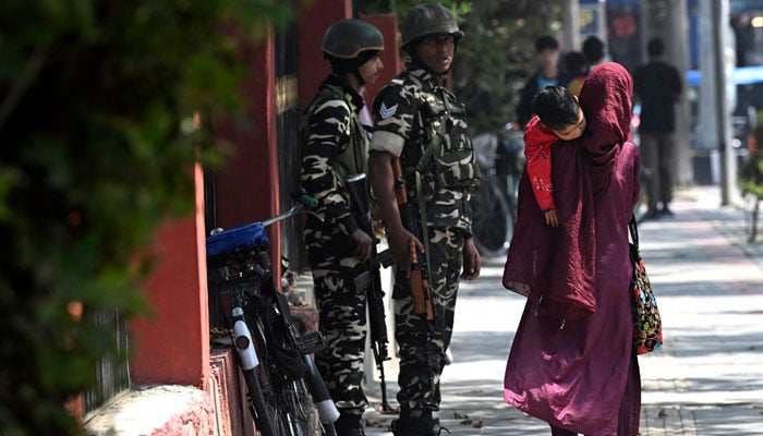 A woman along with a child walks past Indian security personnel on a street in Srinagar, Indian Illegally Occupied Jammu and Kashmir (IIOJK) on September 9, 2024. — AFP