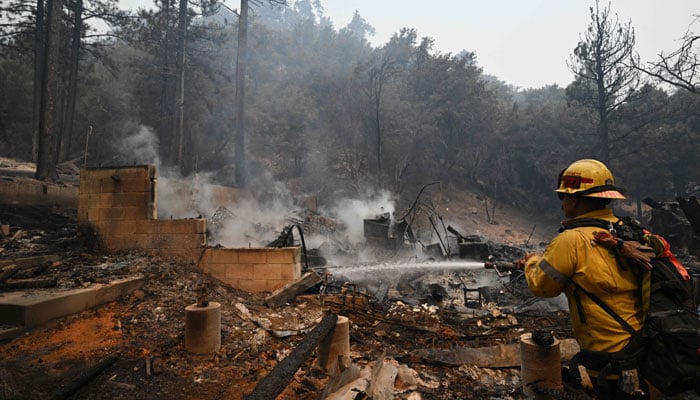 A firefighter uses a hose to extinguish embers in the remains of a home destroyed in the Bridge Fire, in Wrightwood, California on September 11, 2024. — AFP