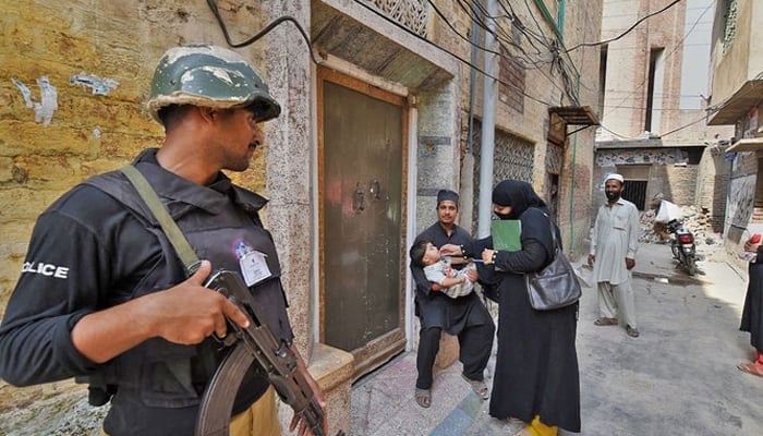 A policeman stands guard as a health worker administers polio drops to a child. — AFP/File