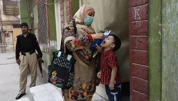 A health worker, escorted by a police officer, administers polio vaccine drops to a child during a vaccination campaign. — AFP/File