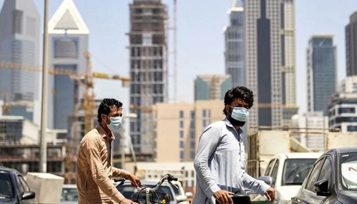 Foreign workers clad in mask walk pushing bicycles along a street in the Satwa district of Dubai on May 6, 2020. — AFP