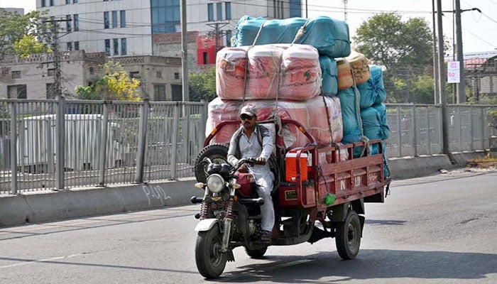 A loader rickshaw driver on his way loaded with a water cooler at Ferozepur Road to deliver to a local market on May 29, 2024. — APP