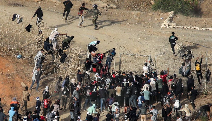 Migrants storm a barbed-wire fence as they attempt to cross the land border with Spains African enclave of Ceuta near Fnideq in northern Morocco on September 15, 2024. — AFP