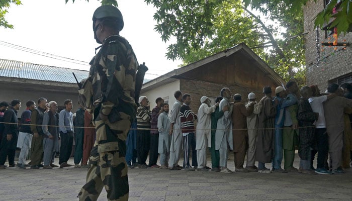 An Indian security personnel stands guard as voters queue up to cast their ballots at a polling station in Pulwama on September 18, 2024. — AFP