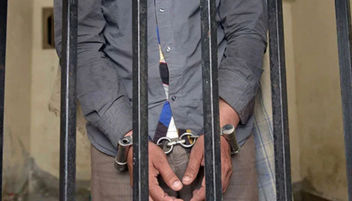 A representational image of a handcuffed person behind bars. — AFP/File