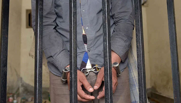 A representational image showing a person handcuffed and standing behind bars. — AFP/File