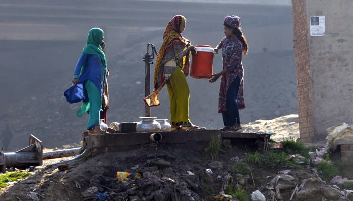 Photo of women filling water in large containers and 1st woman is giving water colar to 2nd woman seen in the outskirts of Lahore. — AFP/File